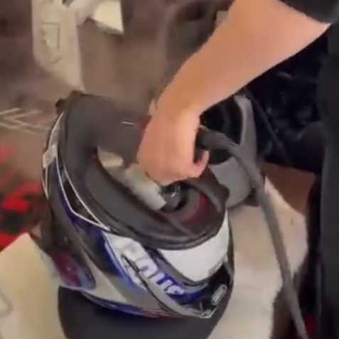 main tenant un nettoyeur vapeur au dessus d'un casque de moto